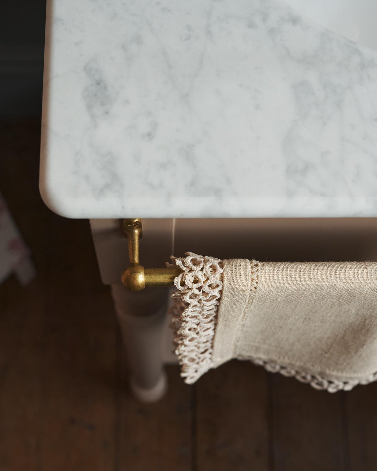 A detailed view of an aged brass towel rail attached to the front of a Victorian-inspired washstand, a vintage lace hand towel hangs from the rail. | Front Towel Rail shown TEST