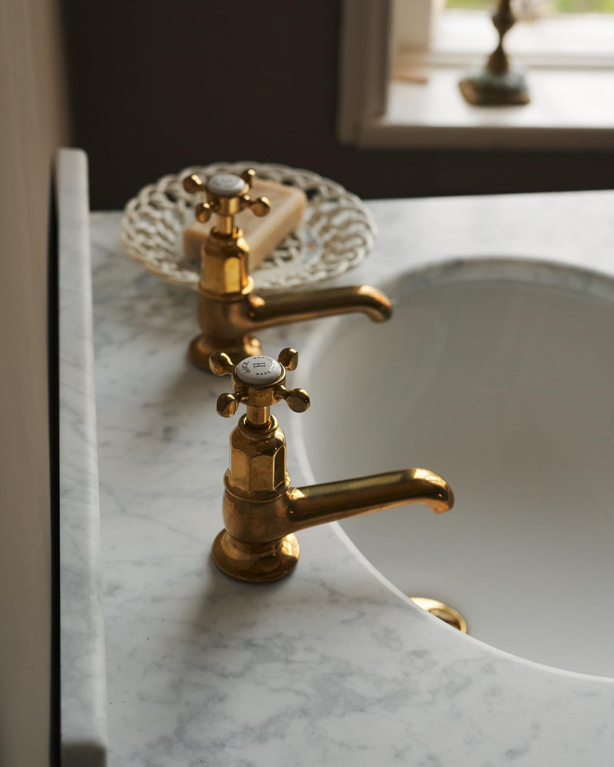 A profile view of a pair of aged brass pillar taps fitted to a bathroom washstand. TEST