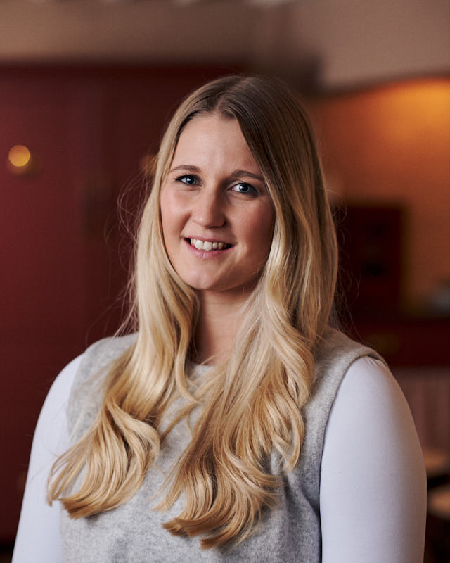 Woman with long blonde hair smiling in a softly lit indoor setting
