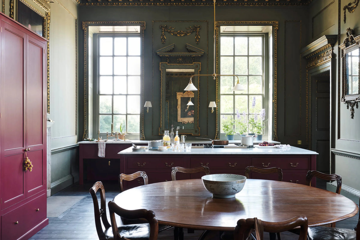 Grand kitchen with wooden dining table and chairs, large windows, and ornate decor.