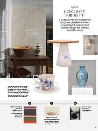 A page of a magazine. The top left half is made up of a lifestyle image of Delft tiles installed on a wall with a wooden table pushed against them. The rest of the page has cut out images of other Delft ceramics and small chunks of black text.