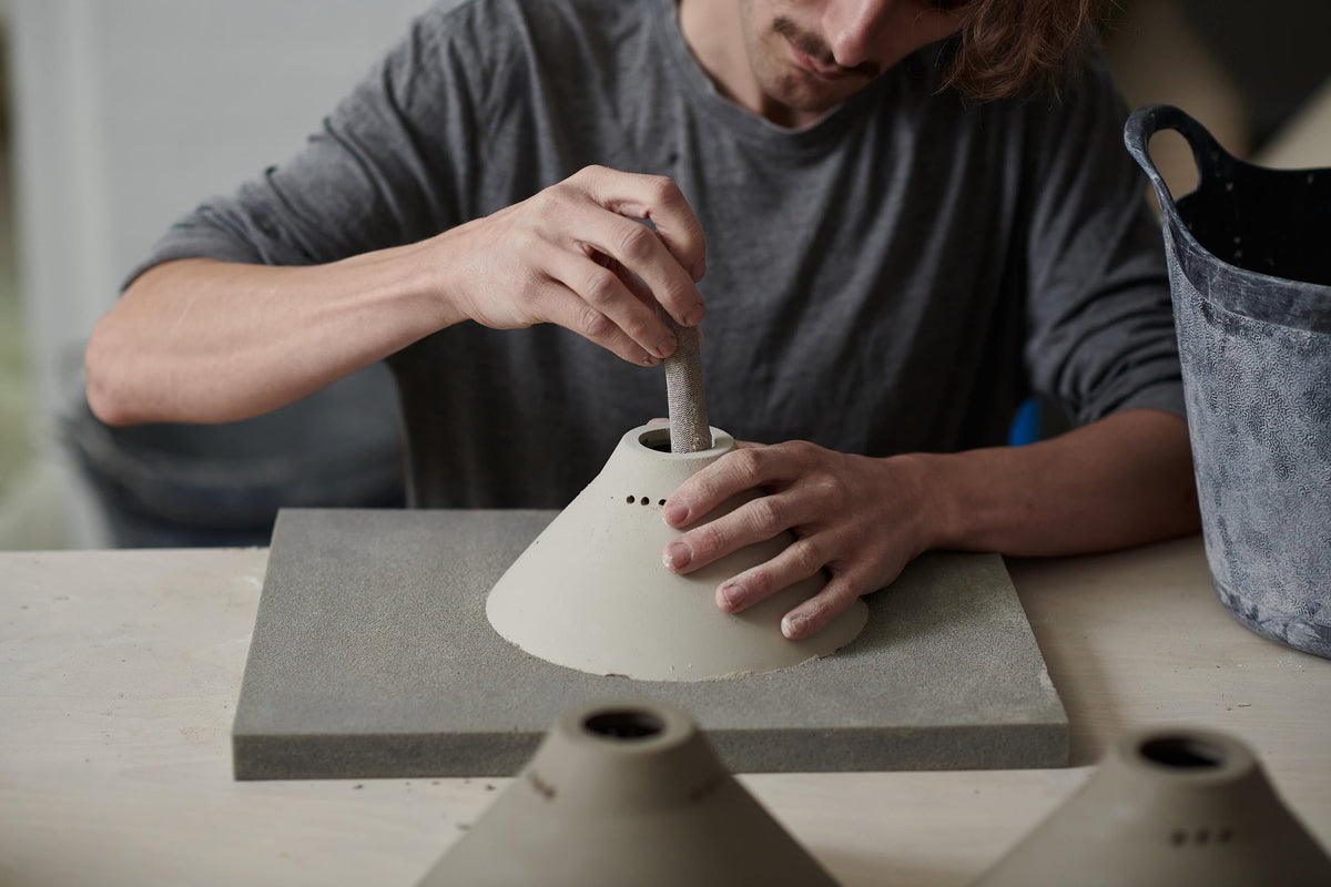 A ceramicist carefully cleaning up the edges of a dry porcelain lamp piece.