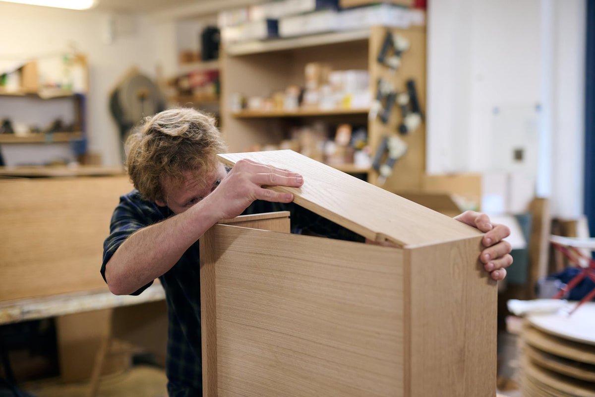 A man carefully placing the final fourth piece of a cupboard in the wood workshop.