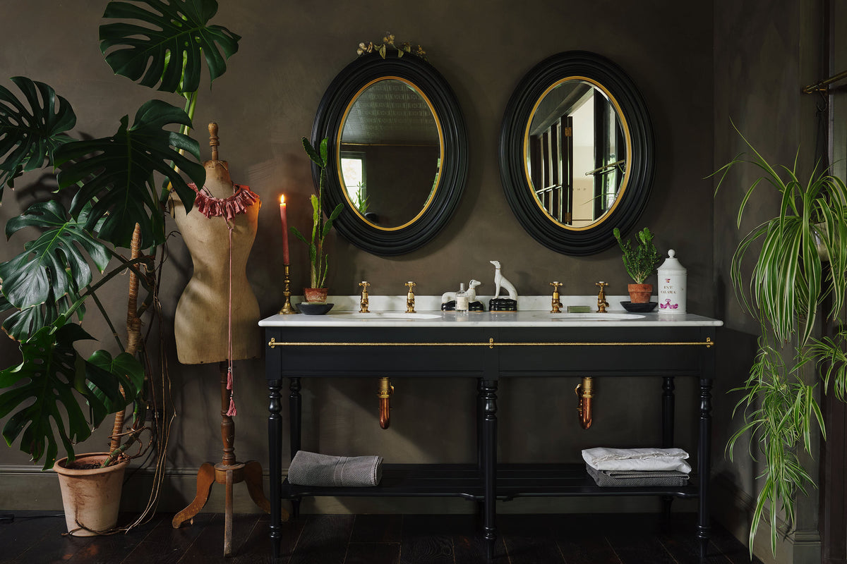 A dark and elegant bathroom that features the printer's black twin wash stand, two matching vintage mirrors, and decorated with a variety of lush green plants.