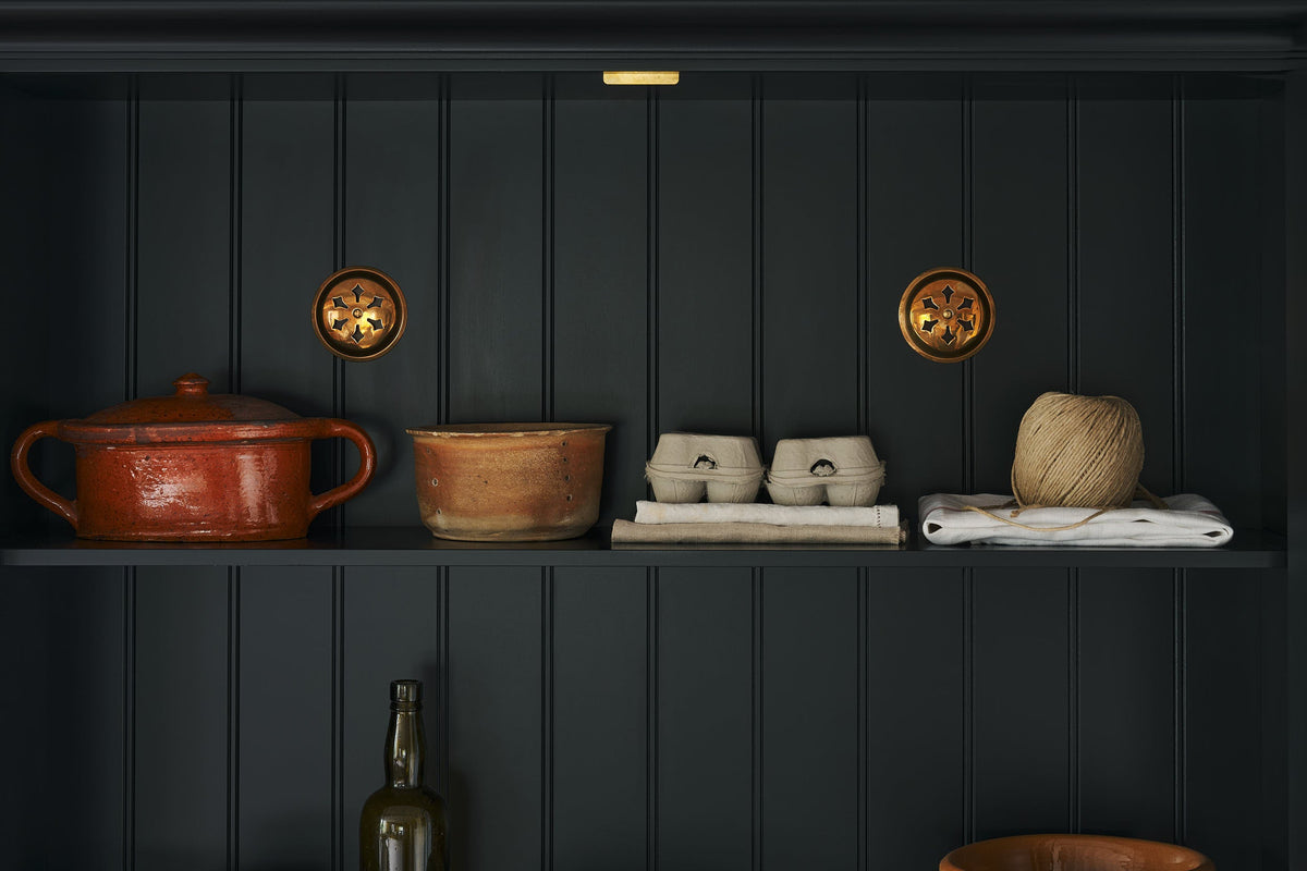 A close-up look inside a pantry cupboard are a pair of brass ventilation grille.