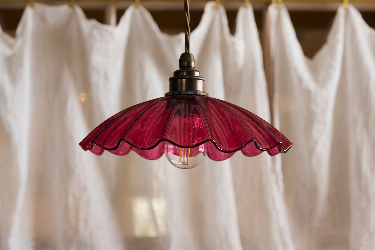 A close-up look at the frilly cranberry glass pendant light with soft white linen curtains behind it.