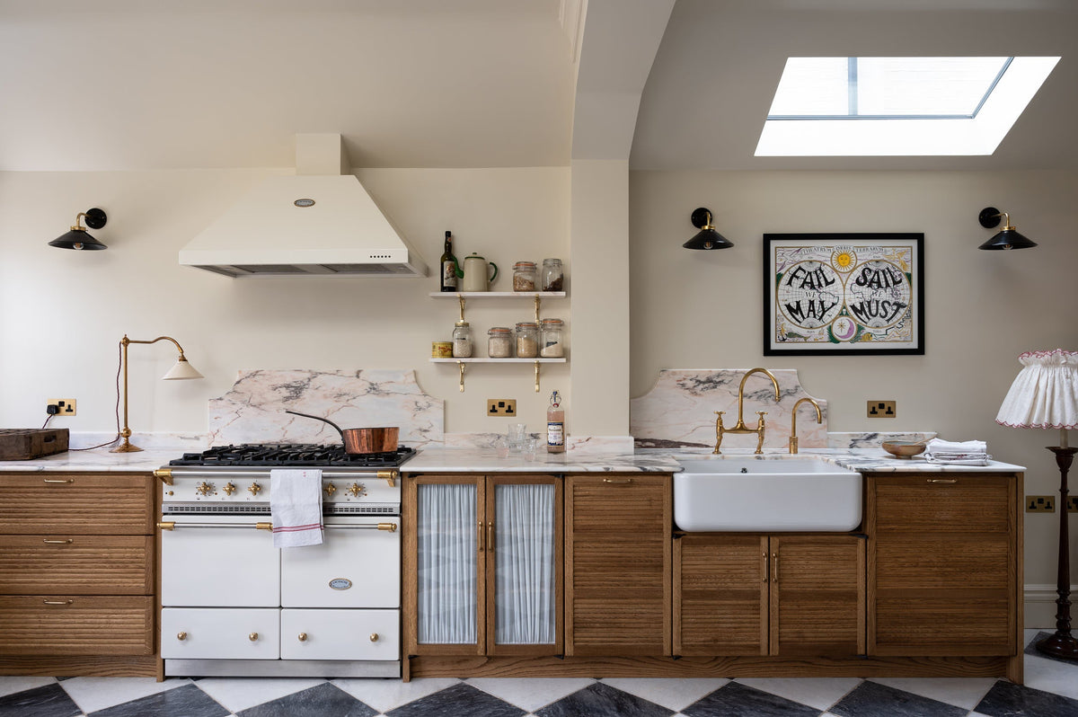 A beautiful white Lacanche cooker flanked by six impressive Haberdasher’s base cupboards, mostly closed with tactile tambour fronts except for a glazed double-door cupboard with delicate ethereal muslin curtains. Sandwiched between pale pink Paonazzo marble worktops and dramatic black and white marble flooring, this kitchen has a subtly luxurious feel.