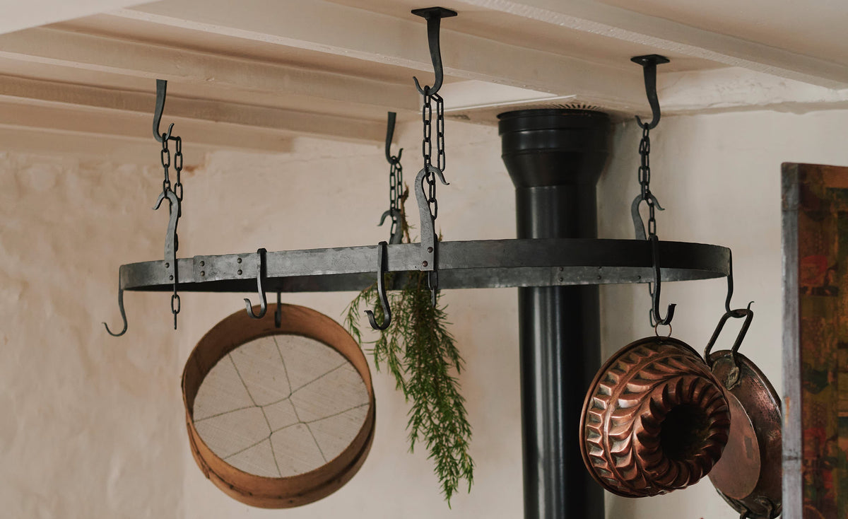 An oblique view of a large oval-shaped wrought iron pot hanger suspended from chains above a black stove cooker.
