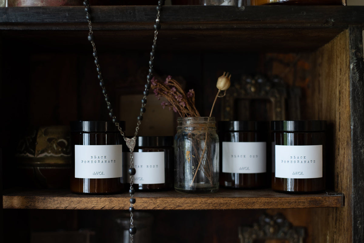 A collection of scented candles in brown glass jars with black lids in a vintage cupboard.