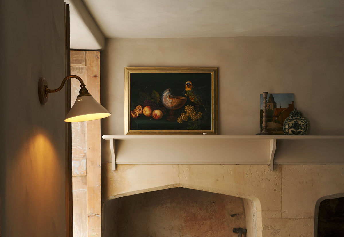 In the quiet corner of a rustic basement kitchen with sandy-coloured walls and ceiling, original Georgian detailing, cream doors and panelling with chipped paintwork and a worn stone floor. An heirloom wall light fits perfectly at home in the ancient and preserved wall.