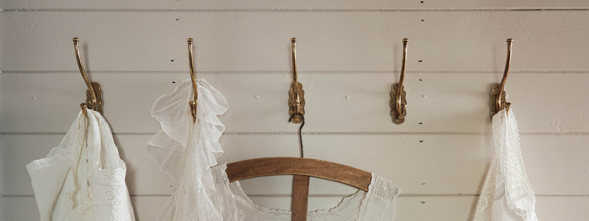 A row of small Parisian café-style brass hooks, fitted to a white painted wall.