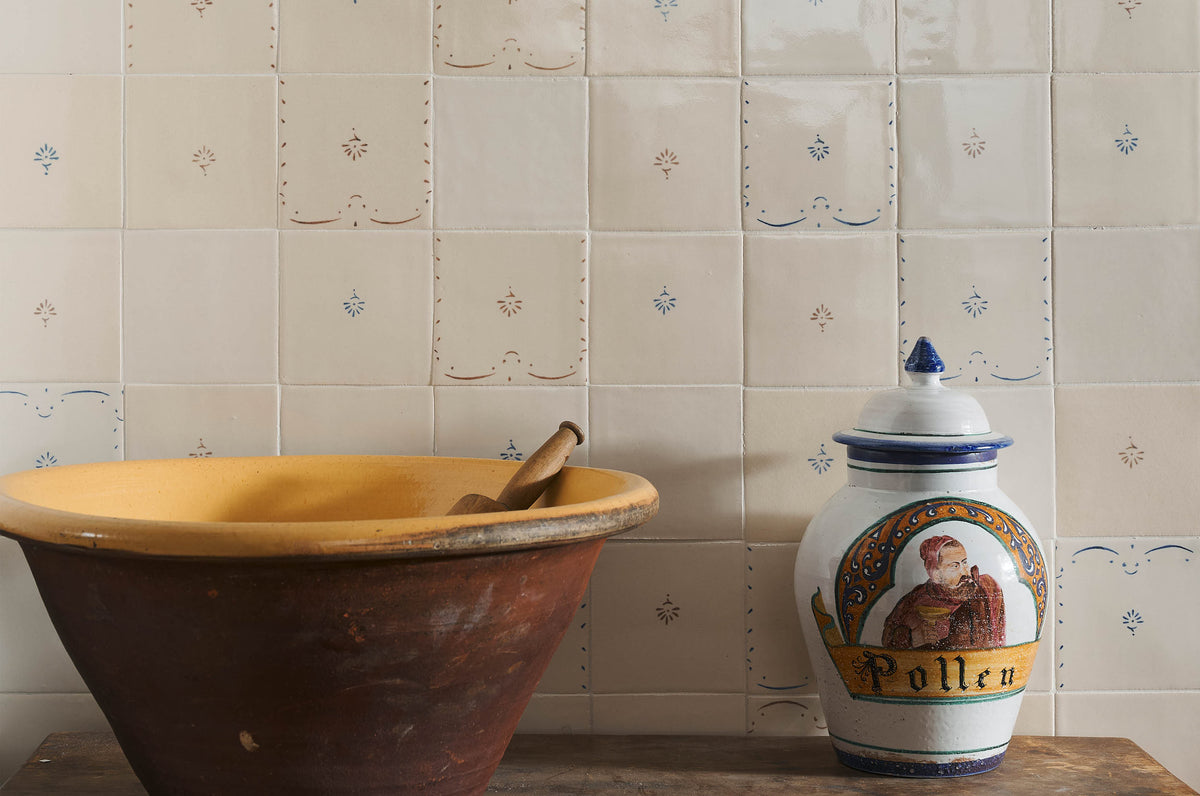 A display of handmade Ditsy Delft Tiles, with a large antique ceramic bowl and painted vase on a wooden table.