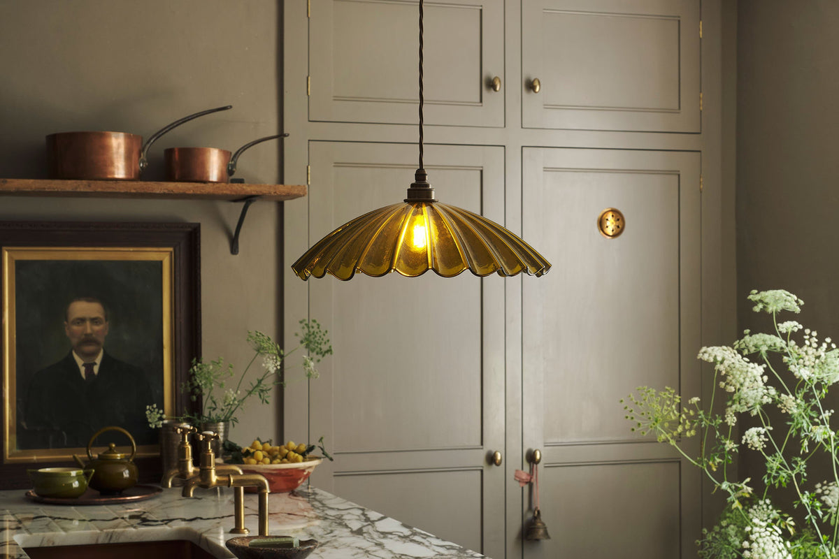 A large chartreuse frilly glass light hanging in a moody grey kitchen.