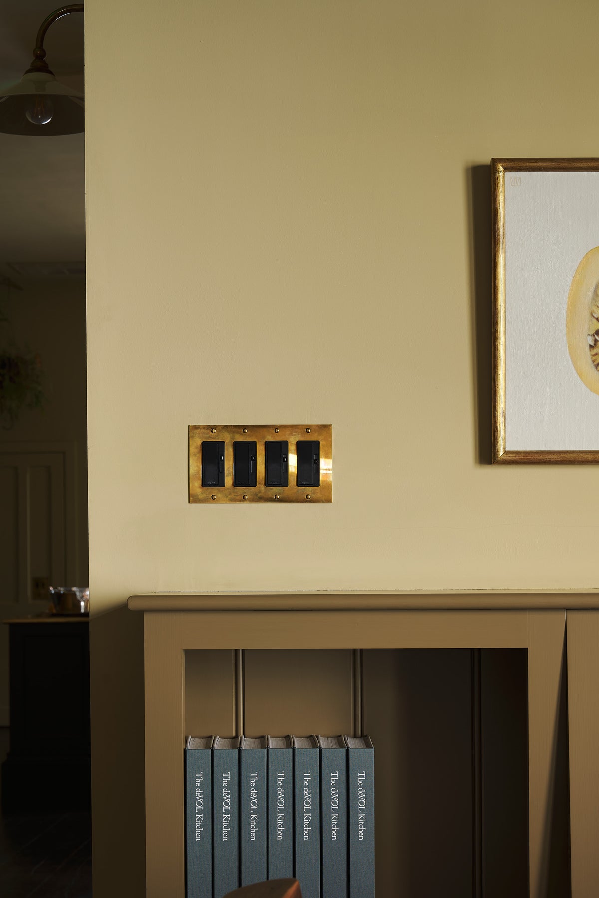 A closer-look at the heirloom brass switches in a yellow room with a glimpse of cupboard showing the deVOL hardback book.