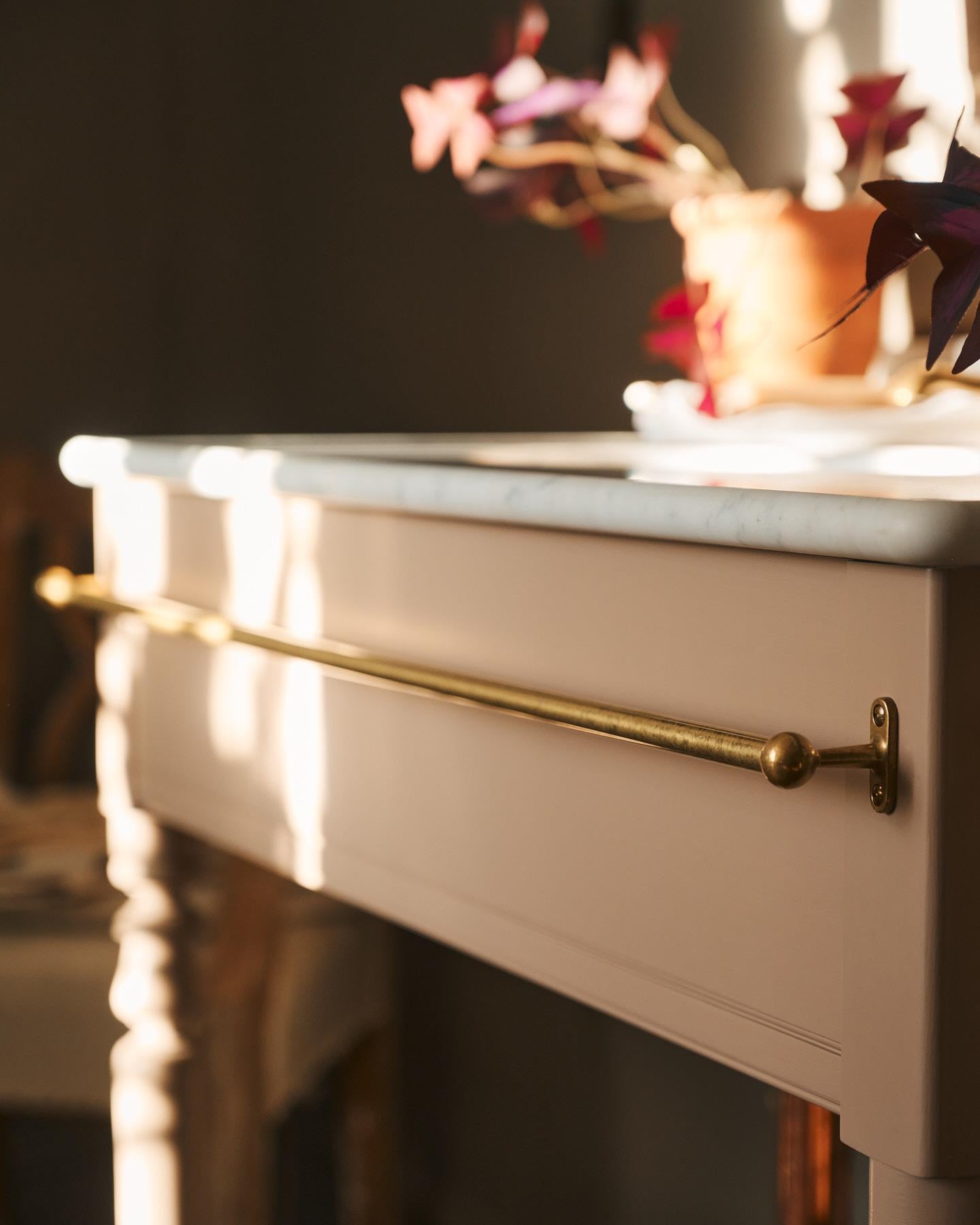 A detailed view of an aged brass towel rail attached to the front of a Victorian-inspired washstand.