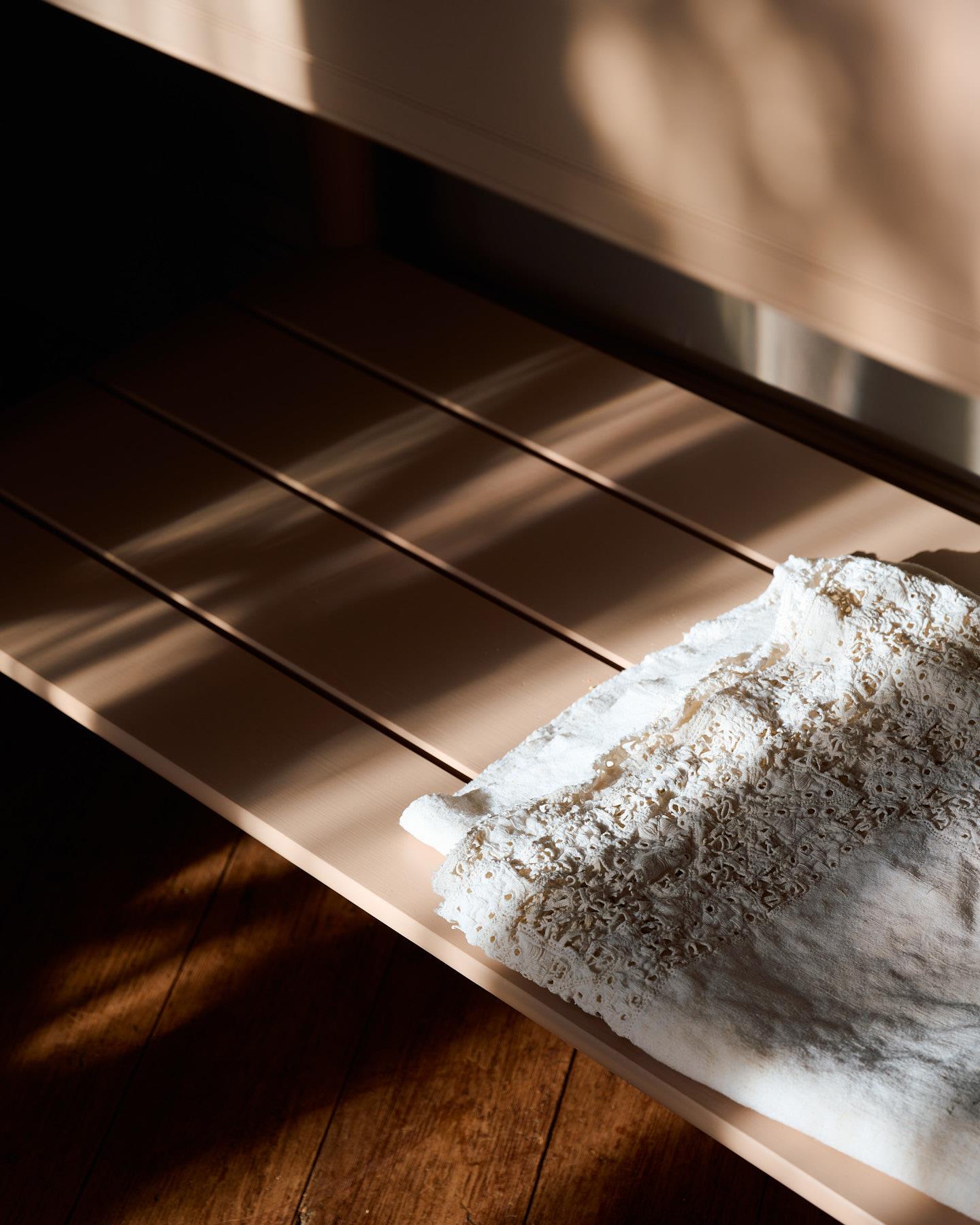 A close-up view of a pink painted slatted shelf at the base of a Victorian-inspired washstand.