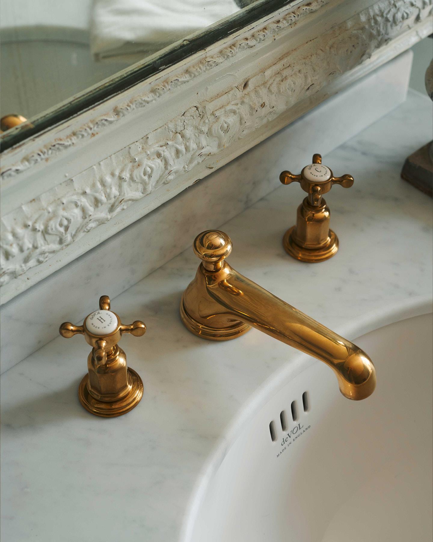 A detailed view of an aged brass towel rail attached to the right side of a Victorian-inspired washstand, a vintage lace hand towel hangs from the rail.