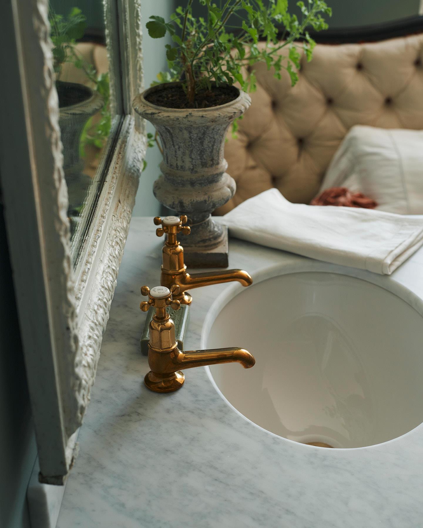 An oblique view of an aged brass pillar taps for a bathroom basin sink fitted to a mushroom painted washstand.