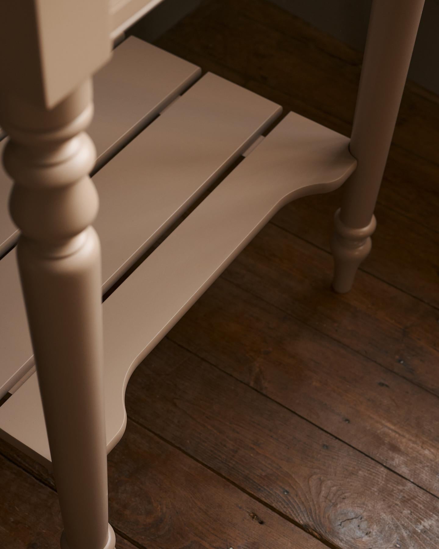 A close-up view of a pink painted slatted shelf at the base of a Victorian-inspired washstand.