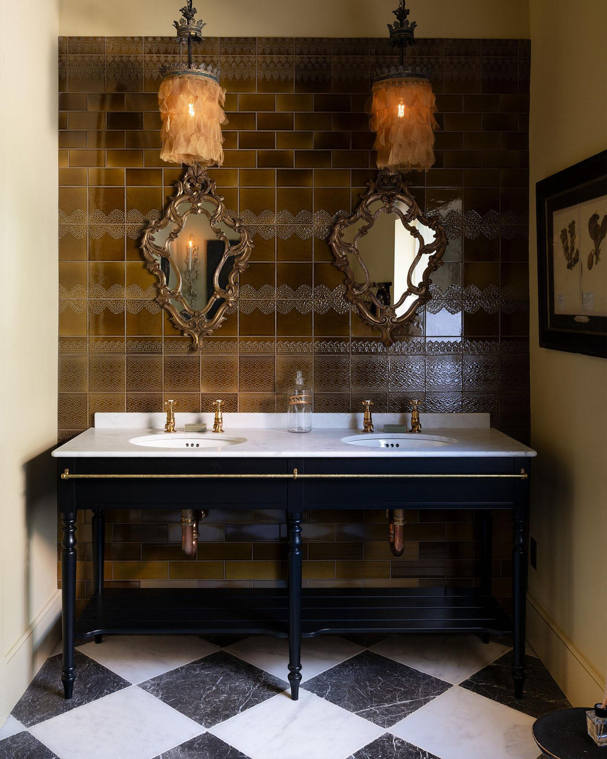 A straight-on view of a grand black Victorian-inspired washstand with two basins and two sets of brass pillar taps. Two antique mirrors and pendant lights sits above the basins. All set against a tall wall of sepia lace market tiles. | Printer's Black shown TEST