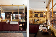 A busy and vibrant Refectory Red Shaker kitchen features an L-shaped sink and cooker run with a Belgian blue limestone worktop, a single fluted Belfast sink, and aged brass Mayan taps. Adorned with vintage items, beloved ceramics, still-life paintings, dried chillies, red lettuce, and an arrangement of berry branches, creates a bright and wonderfully social kitchen space.