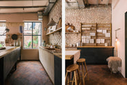 A quiet corner of a calm and simple Sebastian Cox kitchen features a long sink run with two sets of copper sinks and aged brass Mayan taps, a copper worktop, a shelf, and a prep table with a solid oak worktop. Adorned with vintage items, artisan ceramics, wooden chopping boards, tea towels, and wildflowers in large glass containers, this kitchen creates a chic New York industrial space that celebrates a love of natural materials.