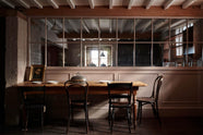 In front of the princelet-pink glazed partition is lovely dining space using an antique solid oak dining table, chairs, artisan ceramics, and a vintage silver cloche.