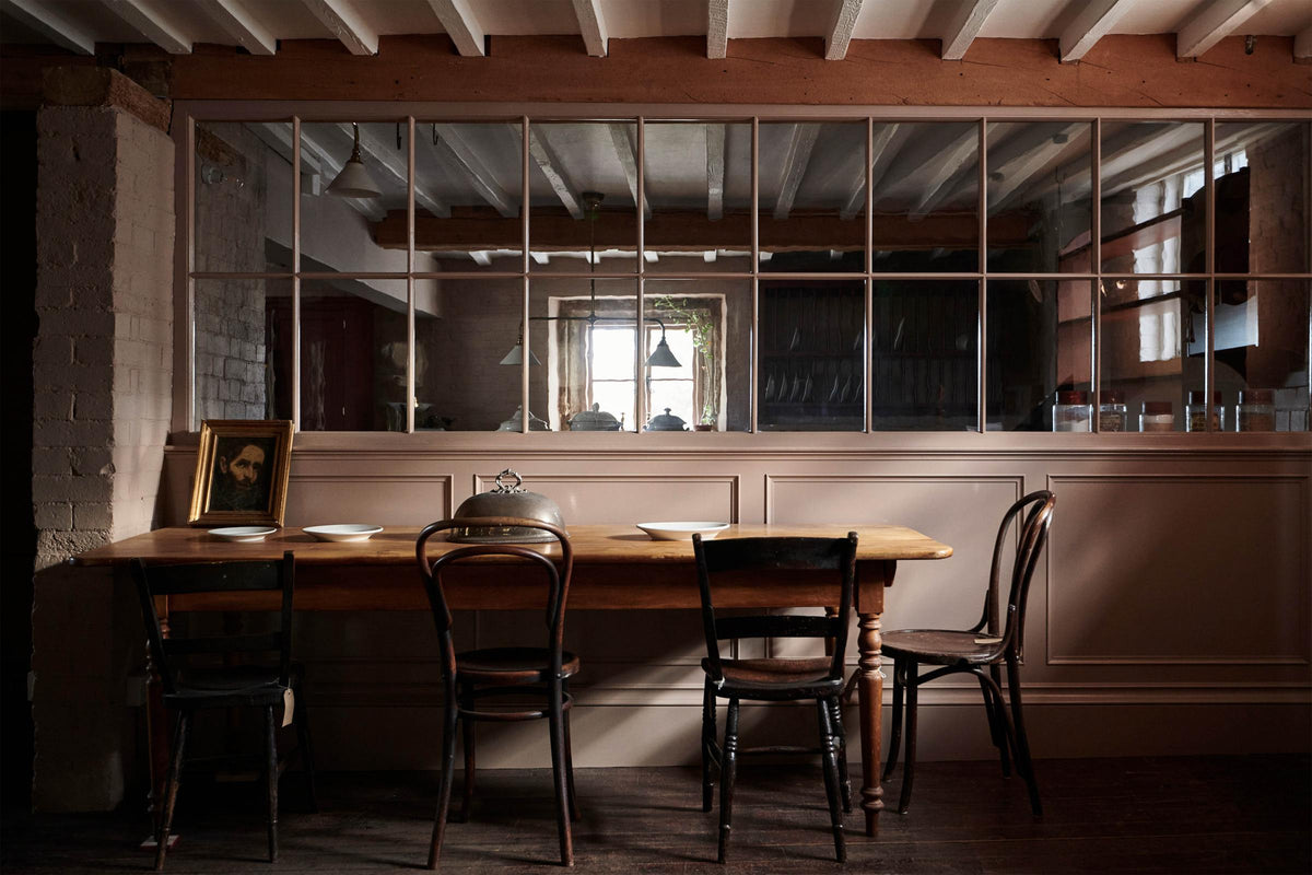 In front of the princelet-pink glazed partition is lovely dining space using an antique solid oak dining table, chairs, artisan ceramics, and a vintage silver cloche.