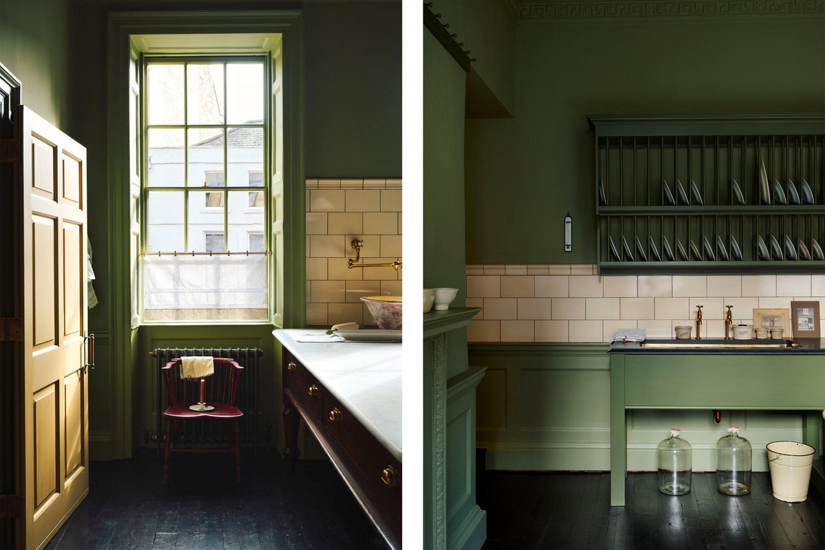 A quaint and stylish Wilkes green Heirloom kitchen features a sink cabinet with a café rail, white lace curtains, a polished brass sink, aged brass Mayan taps, and a large plate rack. Adorned with vintage photos, a cream bucket, simple ceramics, cream subway splashback tiles, and a golden-framed sliced green pumpkin, this kitchen creates a luxurious dining and social space.