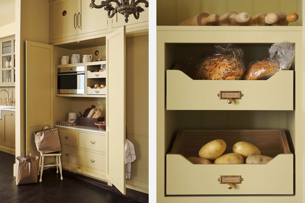 An oblique view of a simple corridor that houses three sets of double cupboards; the left-hand side is open, revealing a pantry cupboard with a microwave. Naturally decorated with a tea towel, artisan ceramics, bread, eggs, potatoes, and an antique chandelier, creating a clean and organised storage space.