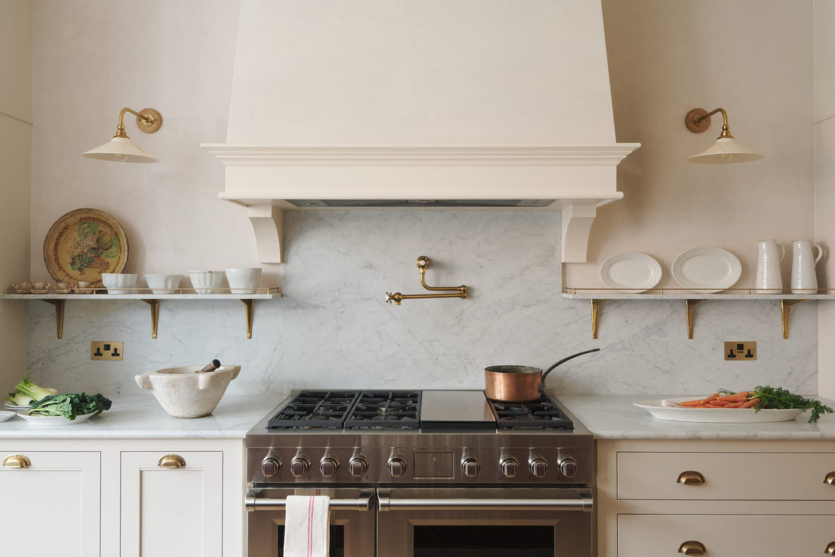 A grand yet understated Classic English kitchen, this space features a dedicated cooker run with a canopy, a full-height cupboard, and an island. Styled with vintage artisan ceramics and a bowl of fresh green pears, it feels wonderfully light, airy, and perfectly suited to relaxed, sociable living.
