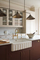 A close and oblique view of a grand yet understated Classic English kitchen, this space features a sink run with reeded glazed wall cupboards, full-height cabinetry, and an island with a Carrara marble worktop. Styled with vintage artisan ceramics and a bowl of fresh green pears, it feels wonderfully light, airy, and perfectly suited to relaxed, sociable living.