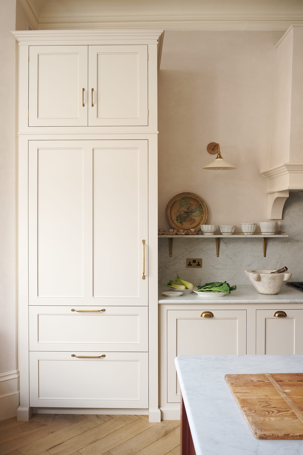 A quiet corner of the grand yet understated Classic English kitchen, this space features a dedicated cooker run with a canopy, a full-height cupboard, and an island. Styled with vintage artisan ceramics, and perfectly suited to relaxed, sociable living.