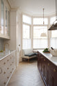 A grand yet understated Classic English kitchen, this space features a sink run with reeded glazed wall cupboards, full-height cabinetry, and an island with a Carrara marble sink. Styled with vintage French copper pans, artisan ceramics, and baskets of fresh fruits and vegetables, it feels wonderfully light, airy, and perfectly suited to relaxed, sociable living.