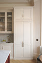 A quiet corner of a grand yet understated Classic English kitchen, this space features a sink run with reeded glazed wall cupboards, full-height, and aged copper cabinetry. Styled with artisan ceramics and a bowl of fresh green pears, it feels wonderfully light, airy, and perfectly suited to relaxed, sociable living.