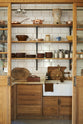 A large haberdasher’s pantry complete with its own haberdasher’s sink run, topped with a marble worktop, large shelves, and an assorted collection of ceramic plates, bowls, pots, pans, and silverware.