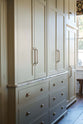 Full-height cabinets with classic brass handles run along one wall and marble worktop. The floor is dark wood, and the walls are covered in creamy white subway tiles. 