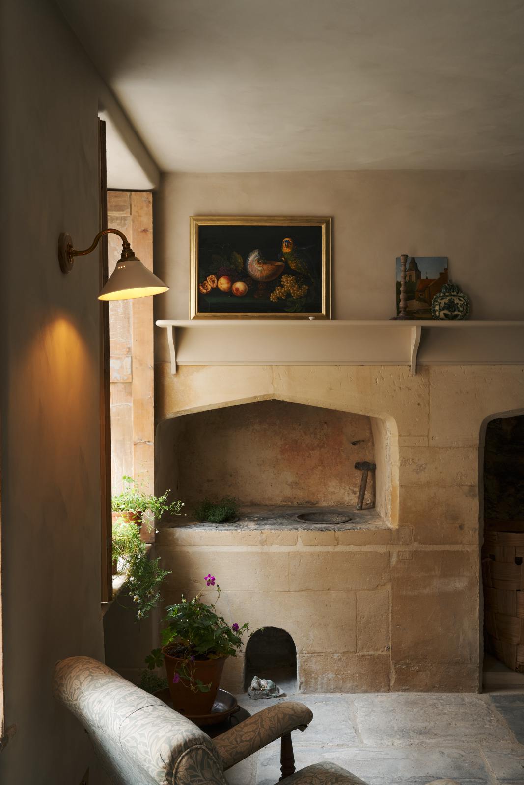 In the quiet corner of a rustic basement kitchen with sandy-coloured walls and ceiling, original Georgian detailing, cream doors and panelling with chipped paintwork and a worn stone floor. An heirloom wall light fits perfectly at home in the ancient and preserved wall.