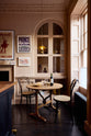 A quiet corner of a bold and dramatic Haberdasher’s kitchen features a deVOL petite vineyard table, Bentwood café chairs, and a petite frilly chartreuse light. Adorned with a delicious bottle of wine, drinking glasses, hors d’oeuvres, quirky framed illustrations and posters, and labelled glass jars, this space creates a local bistro bar atmosphere in Manhattan.