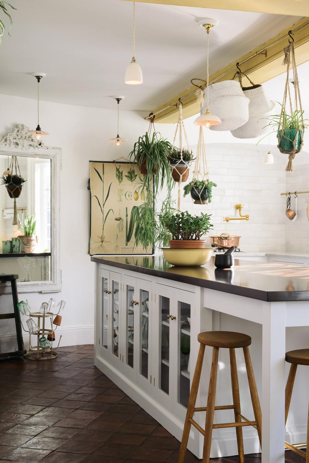 The white linen, classic English kitchen features a large kitchen island with a solid oak worktop, glazed base cabinets, breakfast nook and Helen stools. Lush green hanging plants and white porcelain lights, with the original yellow beam, enhance the bright and cheerful atmosphere, making the kitchen lively and inviting.