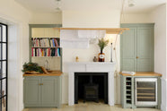 This bright and spacious classic English scullery features a small sink run, a wine cooler, and open and closed counter cupboards topped with solid oak. Adorned with books, artisan ceramics, a deVOL laundry maid, and a bouquet, it creates a delightful mix of simplicity and charismatic personality.