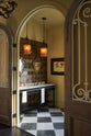 Looking past the antique Parisian doors into a beautiful butter-yellow powder room, you’ll find a black twin Victorian washstand, tall sepia lace market tiles, and a Parisian chequered marble floor. Paired with antique mirrors, pendant lights, and framed pressed botanical artworks, the room exudes a glamorous, vintage charm.