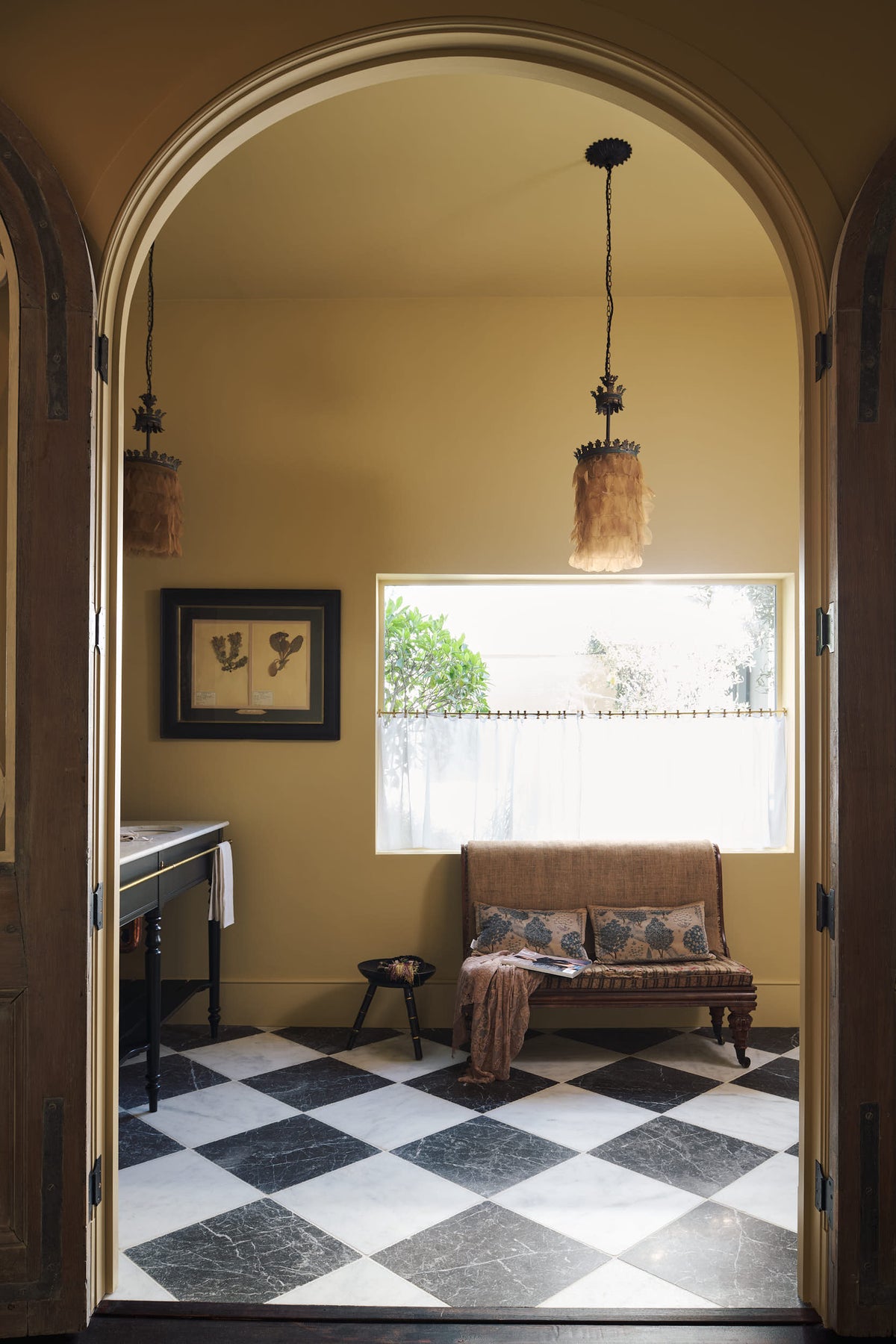 A beautiful butter-yellow powder room, you’ll find a collection of antique furniture, books, magazines, a lace throw, pillows, and a Parisian chequered marble floor.