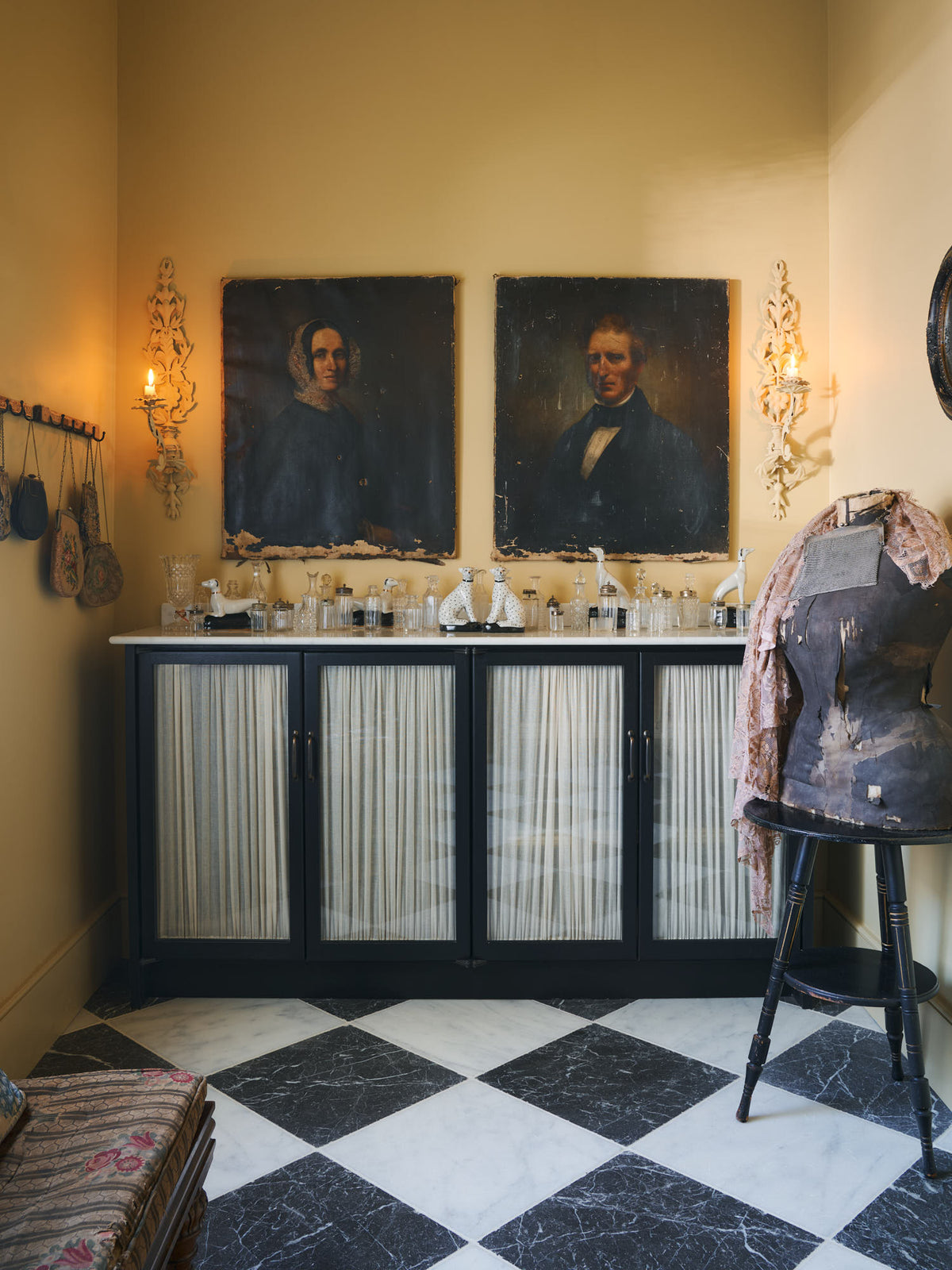 A beautiful butter-yellow powder room, you’ll find a pair of Habedasher’s glazed base cabinets with ruched curtains, a collection of antique furniture, vintage paintings, and a Parisian chequered marble floor. Paired with floral wall candle holders and an old dress form, the room exudes a glamorous, vintage charm.