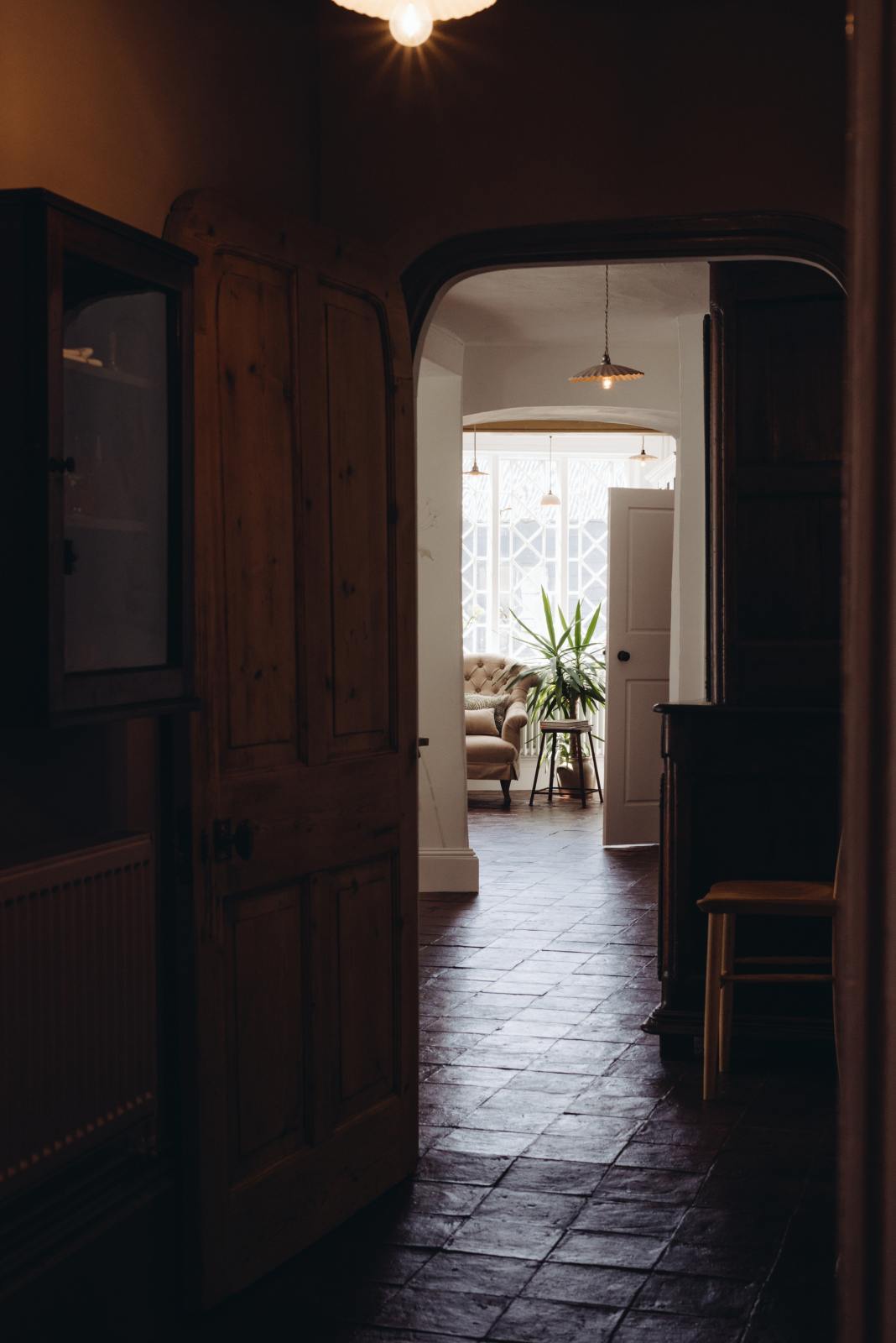 An angled, moody image of an archway, going from a dark and atmospheric corridor towards the white natural light through the Georgian windows. It emphasises the handmade textures of the terracotta square tiles that connect each room, creating a cohesive interior design.