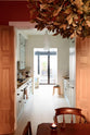 Beyond a cosy wooden dining room featuring a solid oak dining table, chairs, and a detailed oak chandelier, you will find a pale-blue classic English galley kitchen. This leads into a bright, lounging area, adorned with floor-to-ceiling glass windows, allowing plenty of natural light.