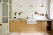 A charming blush yellow, classic English kitchen features a Carrara marble countertop, an ornate backsplash, and an aged brass tap. Decorated with copper pots, vintage ceramics, and small wooden cleaning supplies, it creates an elegant and tidy atmosphere.