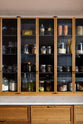 A close-up of a warm and chic Haberdasher’s kitchen features an L-shaped sink and cooker run, countertop cupboards, and a Carrara worktop. Adorned with artisan drinking glasses, dried ingredients in glass jars, clay pots, and vintage items, this kitchen creates a warm and inviting Spanish-inspired space in Yorkshire.