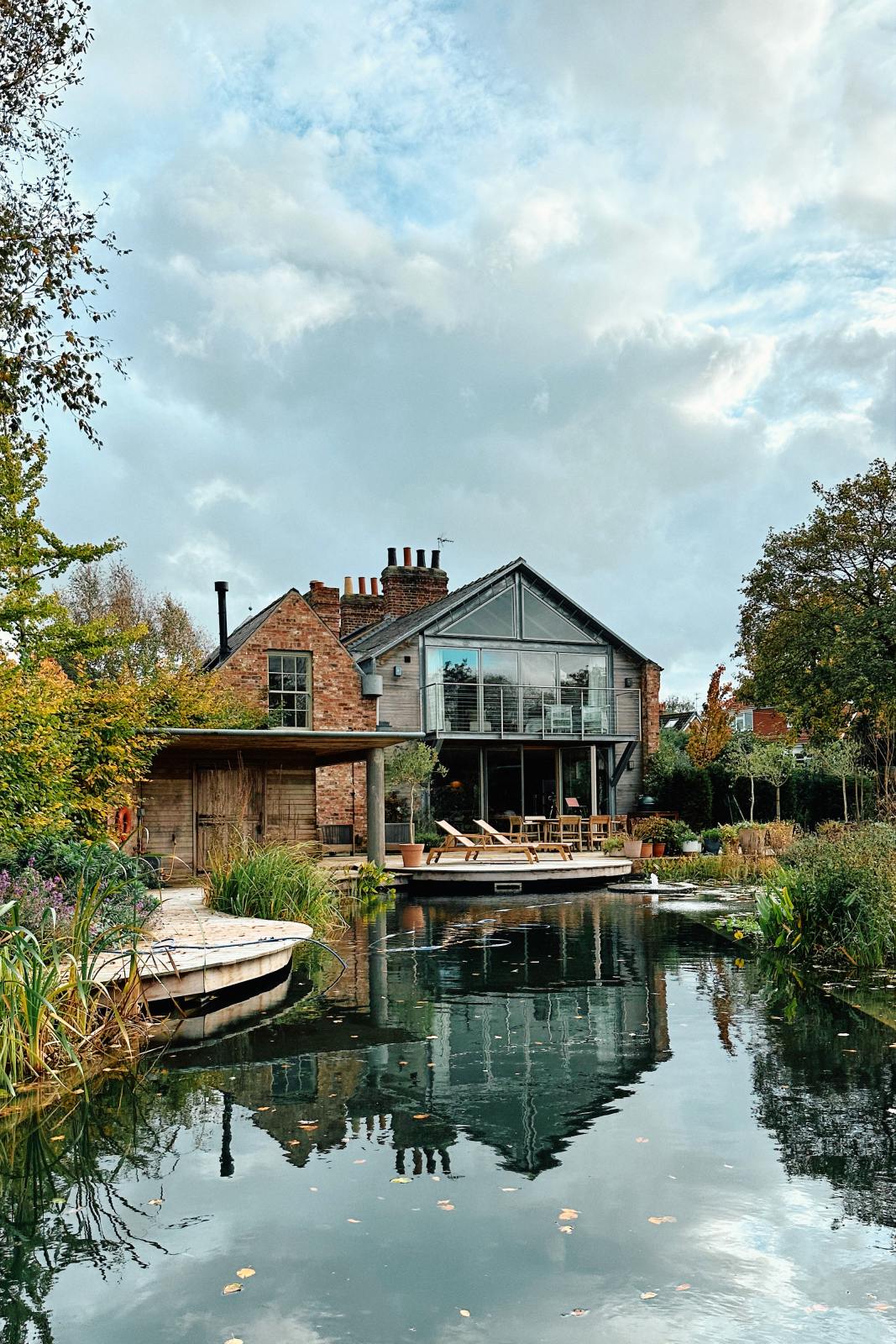 A stylishly remodelled Georgian house boasts a balcony, large French doors, and a spacious pond with fountains, surrounded by luscious fauna.
