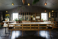 A warm and inviting Haberdasher’s kitchen features a long sink run with a Carrara marble and copper worktop, a double-fluted marble sink, a kitchen island, wall cupboards, and countertop cupboards. Adorned with luscious green hanging and potted plants, vintage items, artisan ceramics, illustrative tea towels, paintings, and a beloved white gas stove, this kitchen creates a lovely exhibitionist space that is both beautiful and practical.